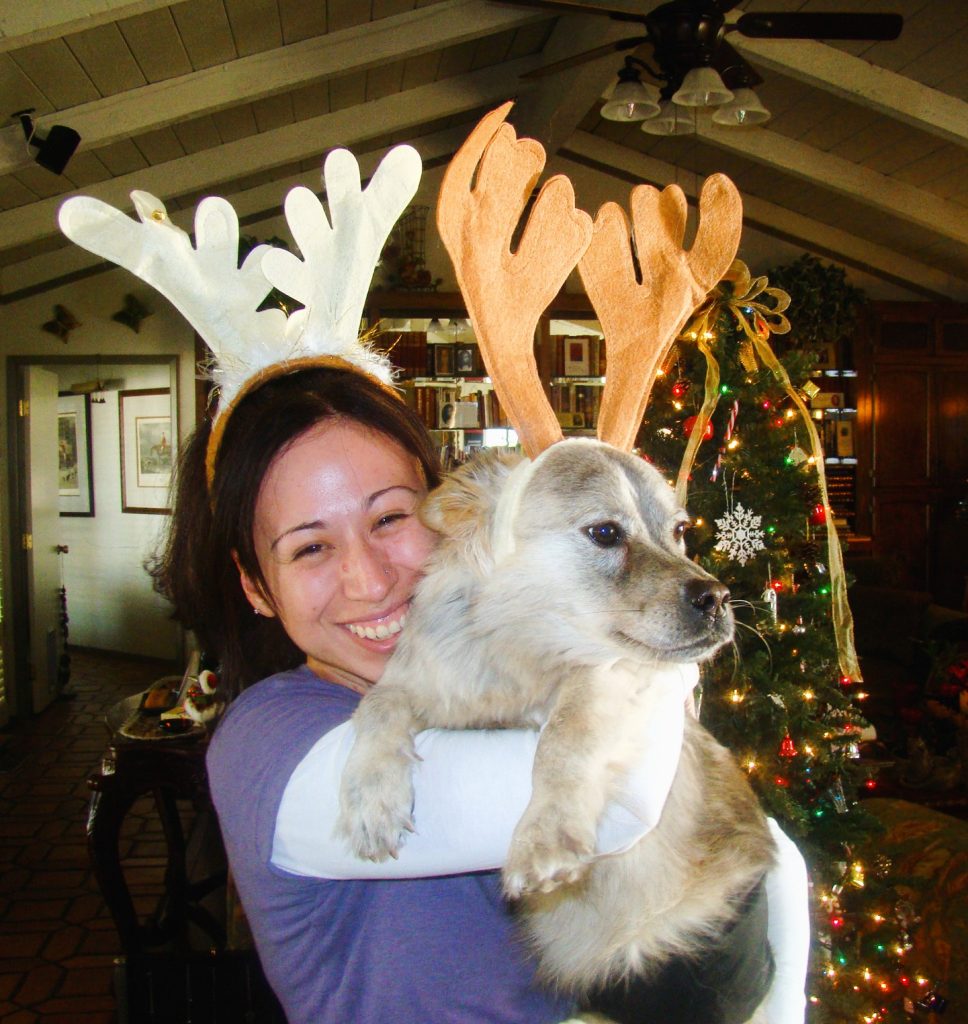woman wearing reindeer headband carrying a dog who is also wearing a reindeer headband