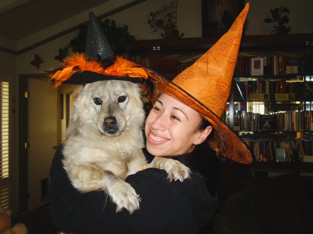 woman wearing witch hat carrying a dog who is also wearing a witch hat