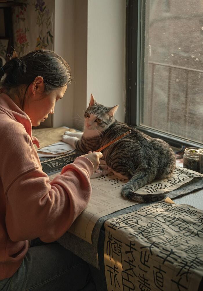A woman focuses on Chinese calligraphy beside a cat in a cozy New York apartment.
