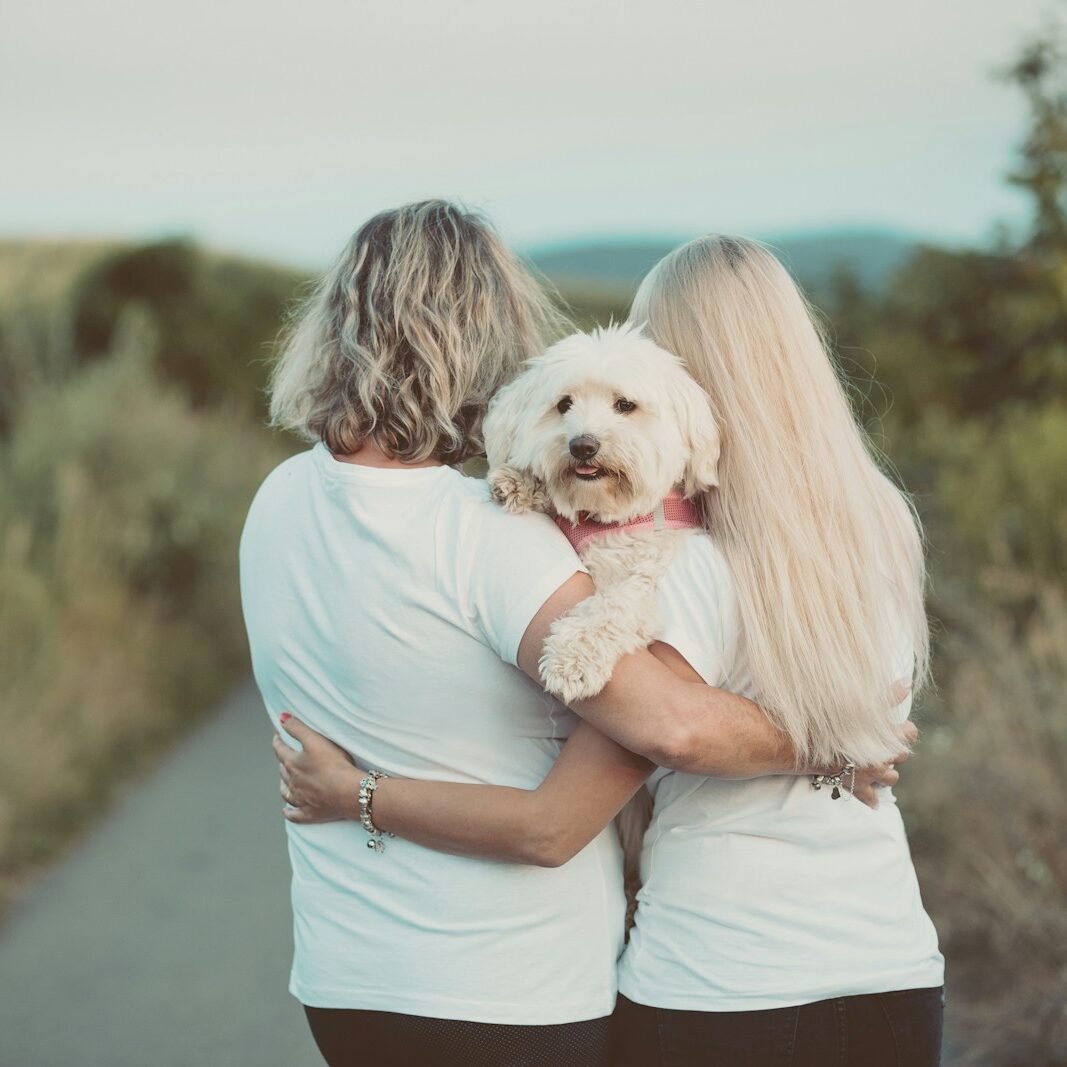 women in white t-shirts hugging white dog